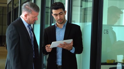 Wall Mural - Two business coworkers discussing in the office corridor while standing and using a digital tablet. Shot in 4k resolution