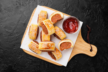 Wall Mural - Delicious homemade sausage rolls served with tomato sauce on a black stone background.