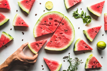 Red slices of ripe watermelon with mint leaves and lime slices on a white background. Top view