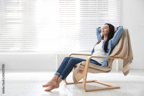 Fotomural Young woman relaxing in armchair near window at home