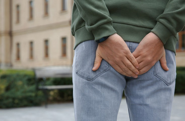 Wall Mural - Man suffering from hemorrhoid pain outdoors, back view