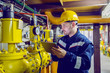 © Dusan Petkovic - Serious caucasian unshaven worker in protective uniform and with hardhat using tablet for checking temperature in pipes. Factory interior.