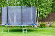 Big trampoline for children and adults. Trampoline with safety net set on green grass beside wooden fence. Green background. Sunny summer day