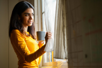 Wall Mural - Persian woman drinking coffee while looking through the window