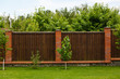 New wooden fence with massive stone brick pillars. Green lawn and trees, daytime