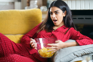 Wall Mural - Persian woman at home watching TV eating chips potatoes