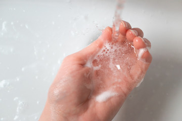 Wall Mural - Washing hand over the sink in the bathroom under water stream with soap foam, close-up. Concept healthcare and hygiene