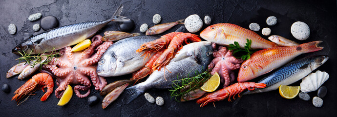 fresh fish and seafood assortment on black slate background. top view.