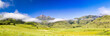 Panorama view of Drakensberg mountains like Cathkin Peak, Monk's Cowl and Champagne Castle with soft and lush green meadows and a blue sky, South Africa