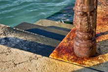 Rusty Pole Serving To Anchor Boats In Front Of Green Sea.