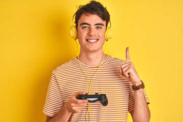 Sticker - Teenager boy playing video games using gamepad over isolated yellow background surprised with an idea or question pointing finger with happy face, number one