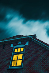 Poster - Intruder with handgun in eerie house with illuminated window under stormy sky at dusk.