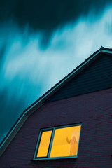 Poster - Intruder with handgun in eerie house with illuminated window under stormy sky at dusk.