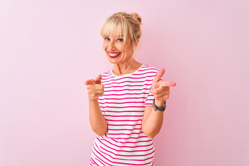 Wall Mural - Middle age woman wearing striped t-shirt standing over isolated pink background pointing fingers to camera with happy and funny face. Good energy and vibes.