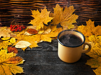Wall Mural - Hot coffee with steam in an enamel mug with leaves on wooden background. Autumn cozy background.