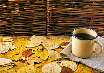 Wall Mural - Hot coffee in an enamel mug on a background of leaves. Autumn cozy background.