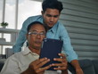 © ake - the lifestyle portrait of  the asian young man son takes care of the old father health and medication in their home and enjoy  mobile technology together