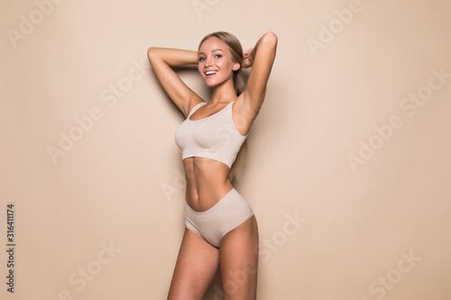 Fototapeta na szkło Młoda kobieta w bieliźnie na beżowym tle. Fitness, dieta, pielęgnacja skóry i ciała