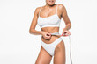 Woman measuring toned waist. Cropped image of woman in white bra and panties measuring her waist while standing isolated on white background