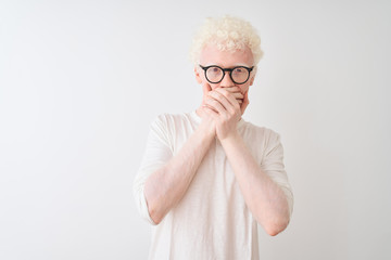 Wall Mural - Young albino blond man wearing t-shirt and glasses standing over isolated white background shocked covering mouth with hands for mistake. Secret concept.