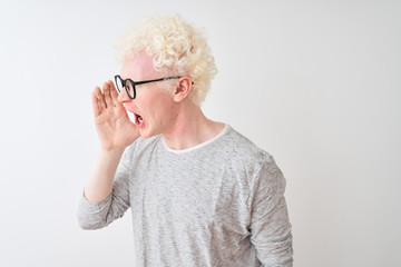 Wall Mural - Young albino blond man wearing striped t-shirt and glasses over isolated white background shouting and screaming loud to side with hand on mouth. Communication concept.