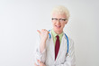 © Krakenimages.com - Young albino doctor man wearing stethoscope standing over isolated white background smiling with happy face looking and pointing to the side with thumb up.