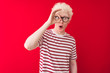 © Krakenimages.com - Young albino blond man wearing striped t-shirt and glasses over isolated red background doing ok gesture shocked with surprised face, eye looking through fingers. Unbelieving expression.
