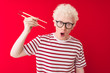 © Krakenimages.com - Young albino blond man holding chopsticks standing over isolated white background scared in shock with a surprise face, afraid and excited with fear expression