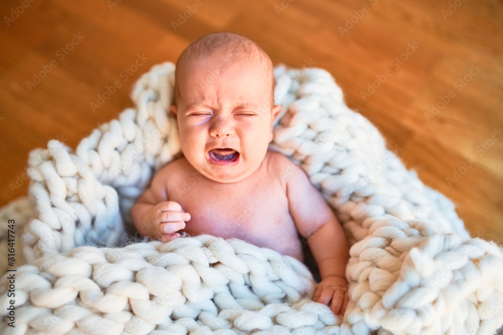 Adorable baby lying down on the floor over blanket at home. Newborn crying - obrazy, fototapety, plakaty 