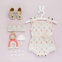 Set of baby clothes and accessories on pink background. Knitted romper with dots on cute hanger with bunny ears and shoes, cotton crown and toys. Fashion newborn. Flat lay, top view