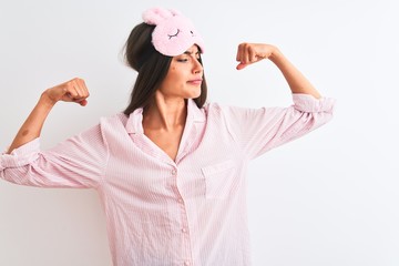 Wall Mural - Young beautiful woman wearing sleep mask and pajama over isolated white background showing arms muscles smiling proud. Fitness concept.