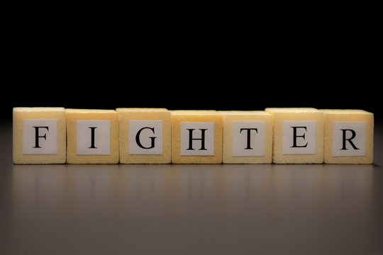 The word FIGHTER written on wooden cubes isolated on a black background..