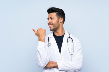 Young doctor man over isolated blue wall pointing to the side to present a product