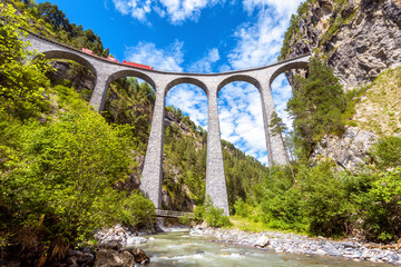 Landwasser Viaduct, Switzerland. Red train runs on high railroad bridge in mountains. This place is landmark of Swiss Alps. Scenic view of famous railway.