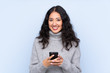 © luismolinero - Spanish Chinese woman over isolated blue background sending a message with the mobile