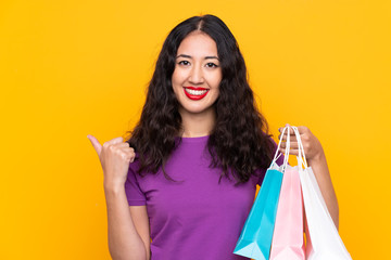 Wall Mural - Spanish Chinese woman with shopping bag over isolated background pointing to the side to present a product