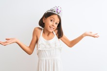 Beautiful Child Girl Wearing Princess Crown Standing Over Isolated White Background Clueless And Confused Expression With Arms And Hands Raised. Doubt Concept.