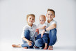 Happy sisters and brother are sitting on the floor on a white background. Two teens and a baby 1 year.