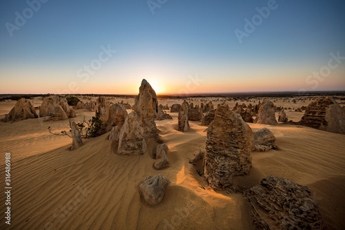 Fototapeta na szkło Słońce za wapiennymi stosami na pustyni Pinnacles w parku narodowym Nambung położonym na północ od Perth w Australii Zachodniej