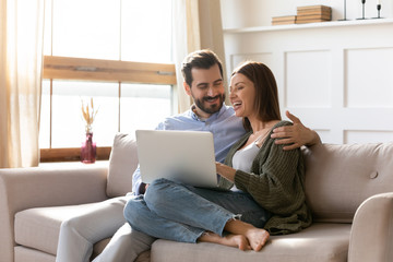 Wall Mural - Young couple rest on sofa browsing internet on modern laptop