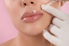 Young Woman Getting Lips Injection On Pink Background, Closeup
