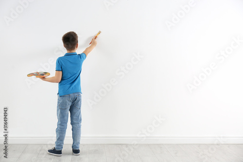 Fotomural Little child painting on white wall indoors. Space for text