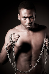 Young half naked african man standing and holding massive chains in hands