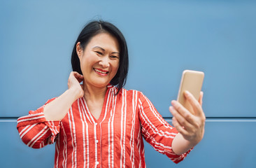 Canvas Print - Happy Asian woman using mobile smartphone outdoor - Senior having fun with new trendy technology for social media apps - Elderly lifestyle tech and aged people concept