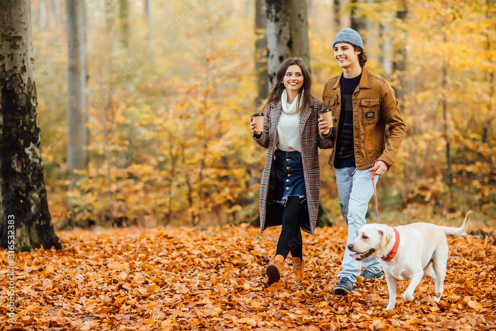 Family and hot autumn drink, couple in love holding cups of tea or coffee and holding hands, walking with dog. - obrazy, fototapety, plakaty 