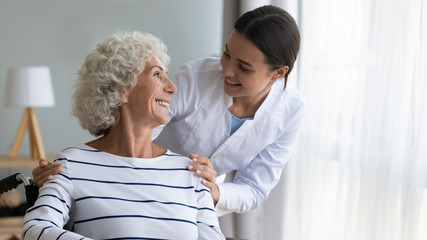 Wall Mural - Smiling caregiver caring about happy disabled older woman in wheelchair