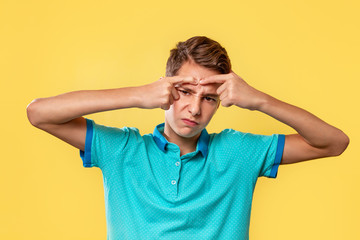 Wall Mural - Cosmetology, Dermatology and acne. Caucasian teenager in a blue t-shirt, painfully squeezes out a pimple on his forehead. Yellow background. Copy space