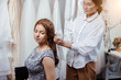 © alfa27 - careful designer in white shirt choose veil for beautiful client sitting in salon among wedding dresses, future fiancee