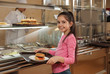 © New Africa - Little girl with plastic tray and burger near serving line in canteen. School food