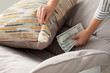 Woman hiding dollar banknotes under pillow on armchair indoors, closeup. Money savings